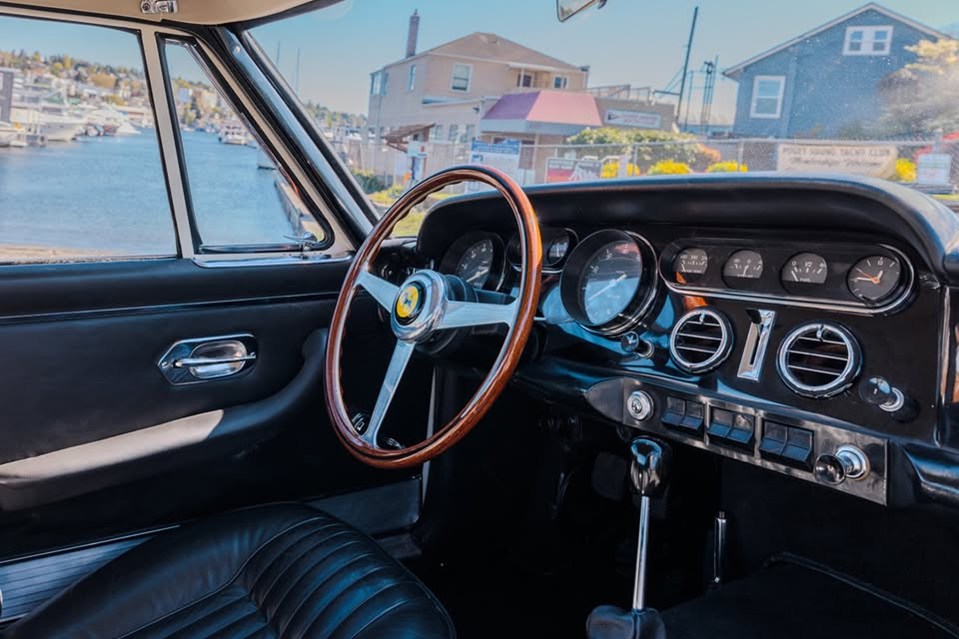 The interior is all black, with a wooden steering wheel and a chrome dashboard