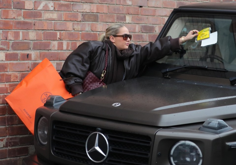 Molly pictured taking her latest parking ticket off her windscreen after her £200k car was spotted by a warden